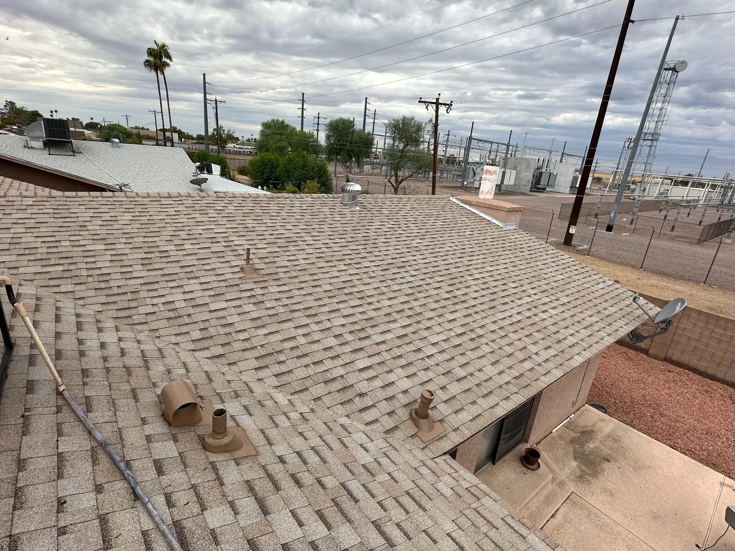 Wide view of a shingle roof with pipe boots and a turbine vent under a cloudy sky